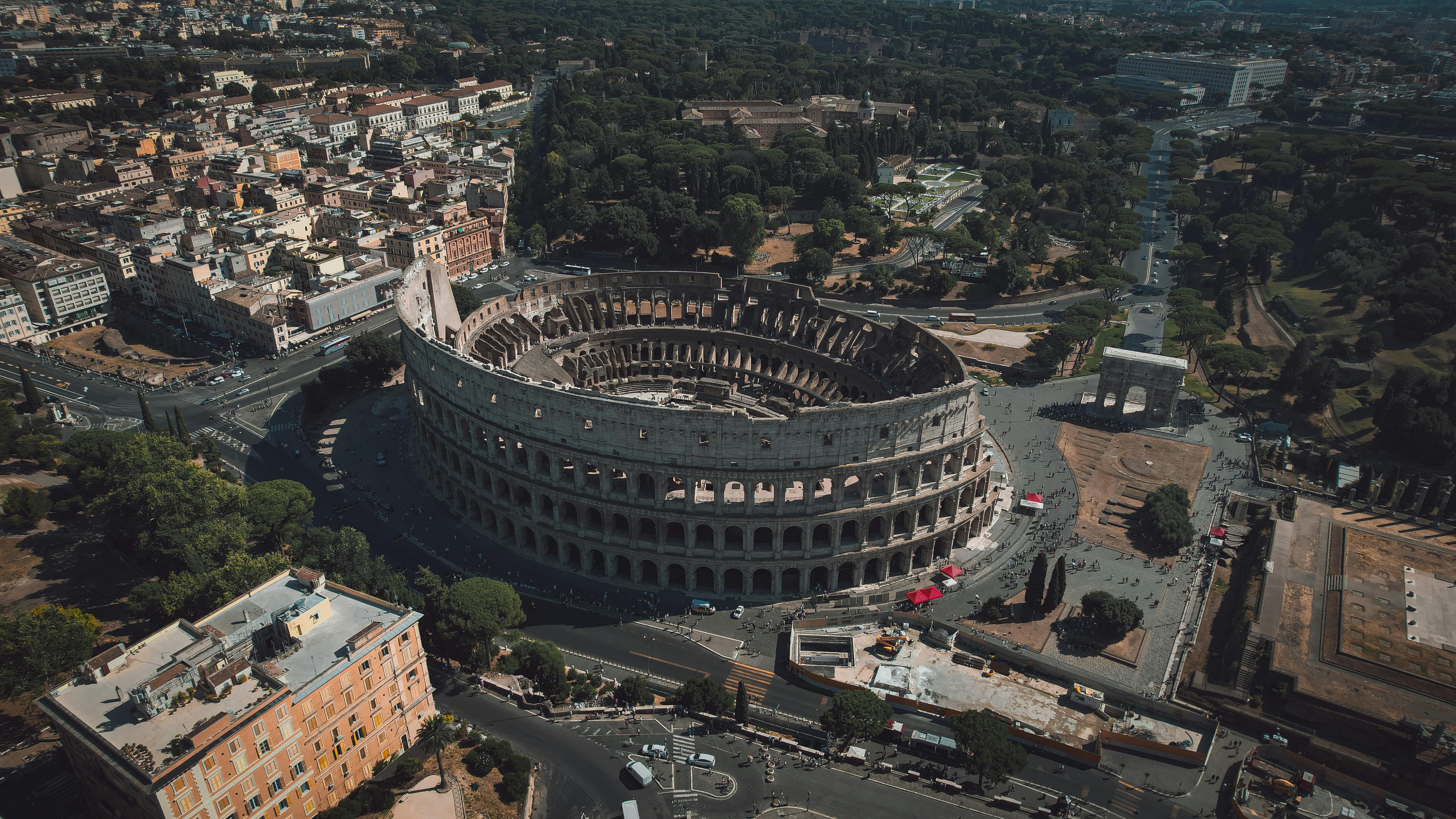 High angle drone shot of the Colosseum in Rome, Italy, showcasing its grandeur and surrounding urban landscape.