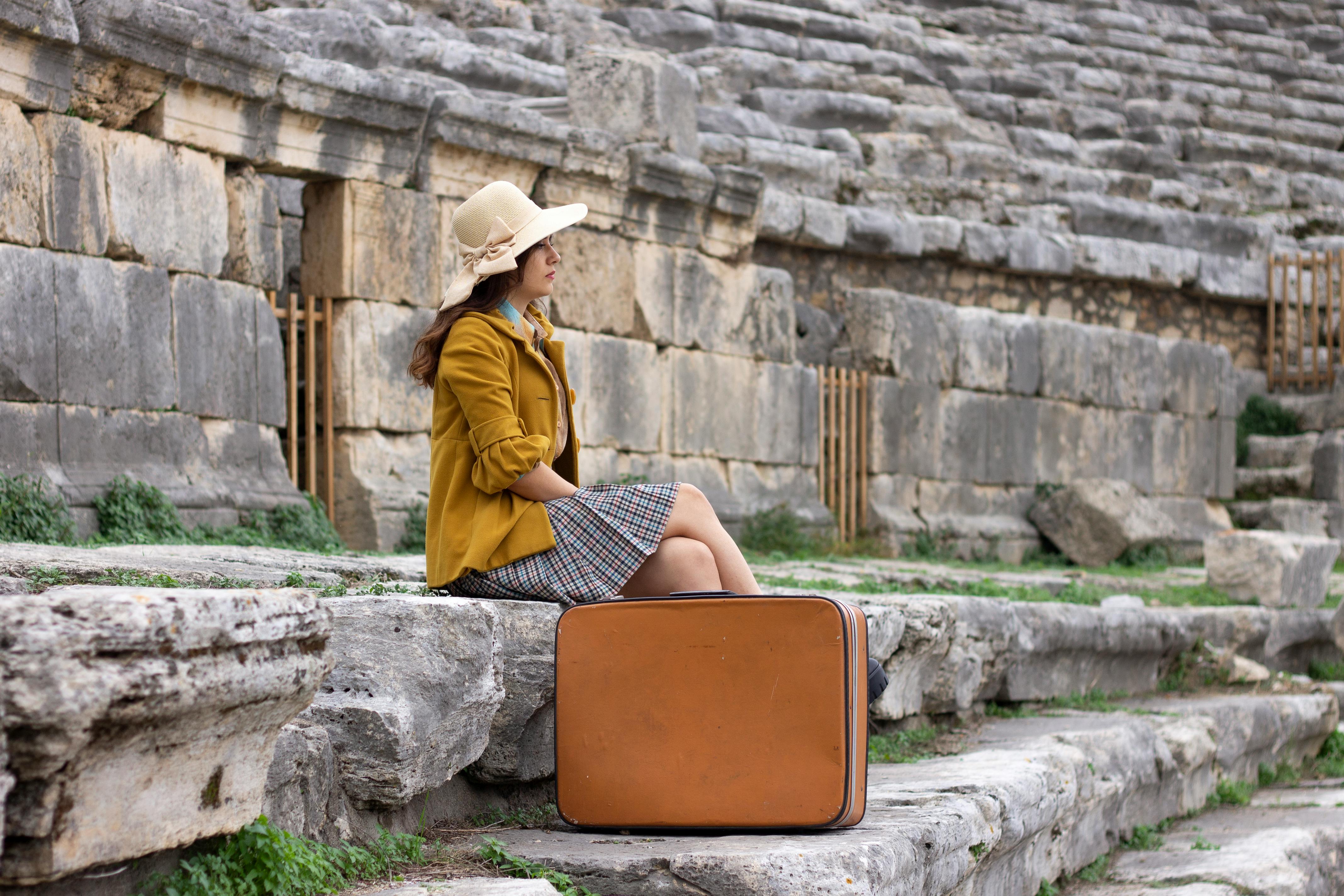 Woman in vintage attire sitting on ancient stone steps with suitcase in Türkiye